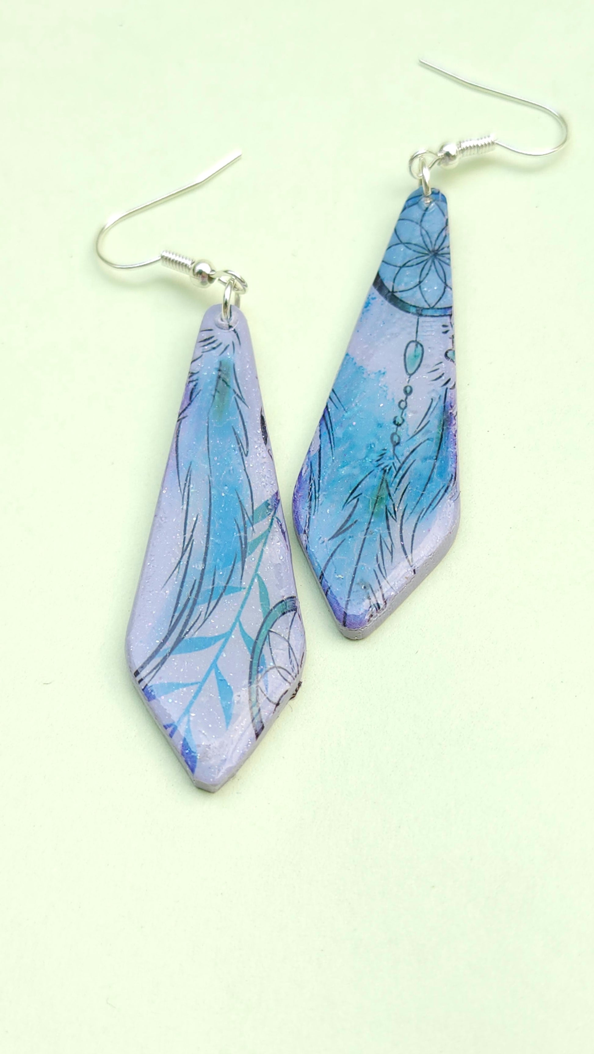 Pair of blue and purple leaf-patterned earrings on a light green background